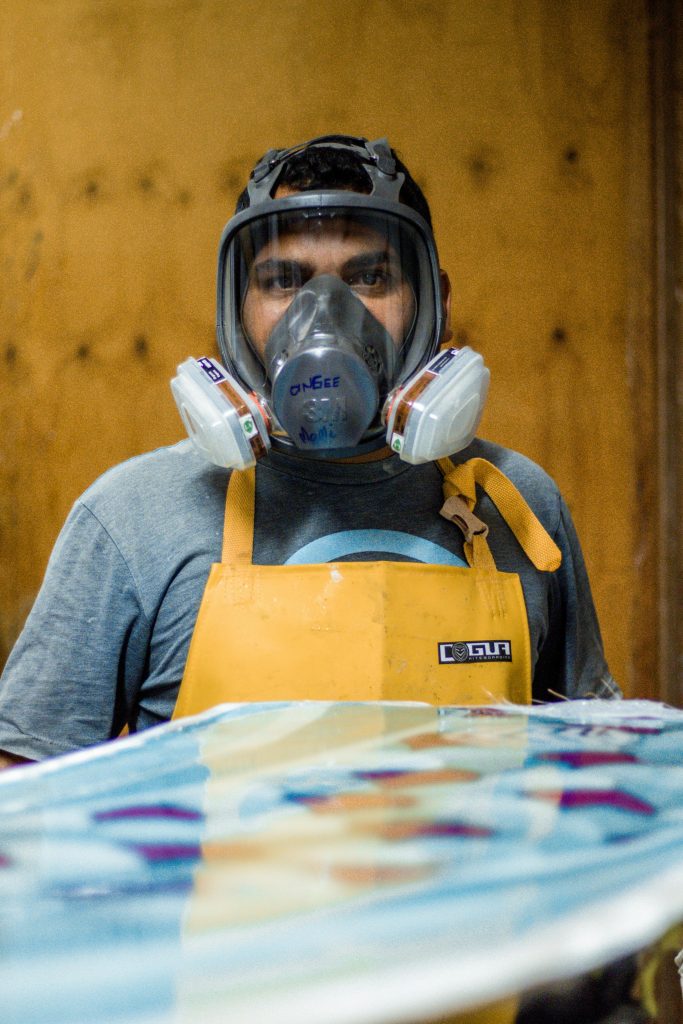 A worker in protective gear stands focused in a workshop environment.