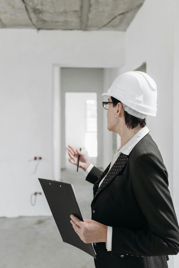 A professional engineer in a suit and hard hat inspecting a construction site with a clipboard.